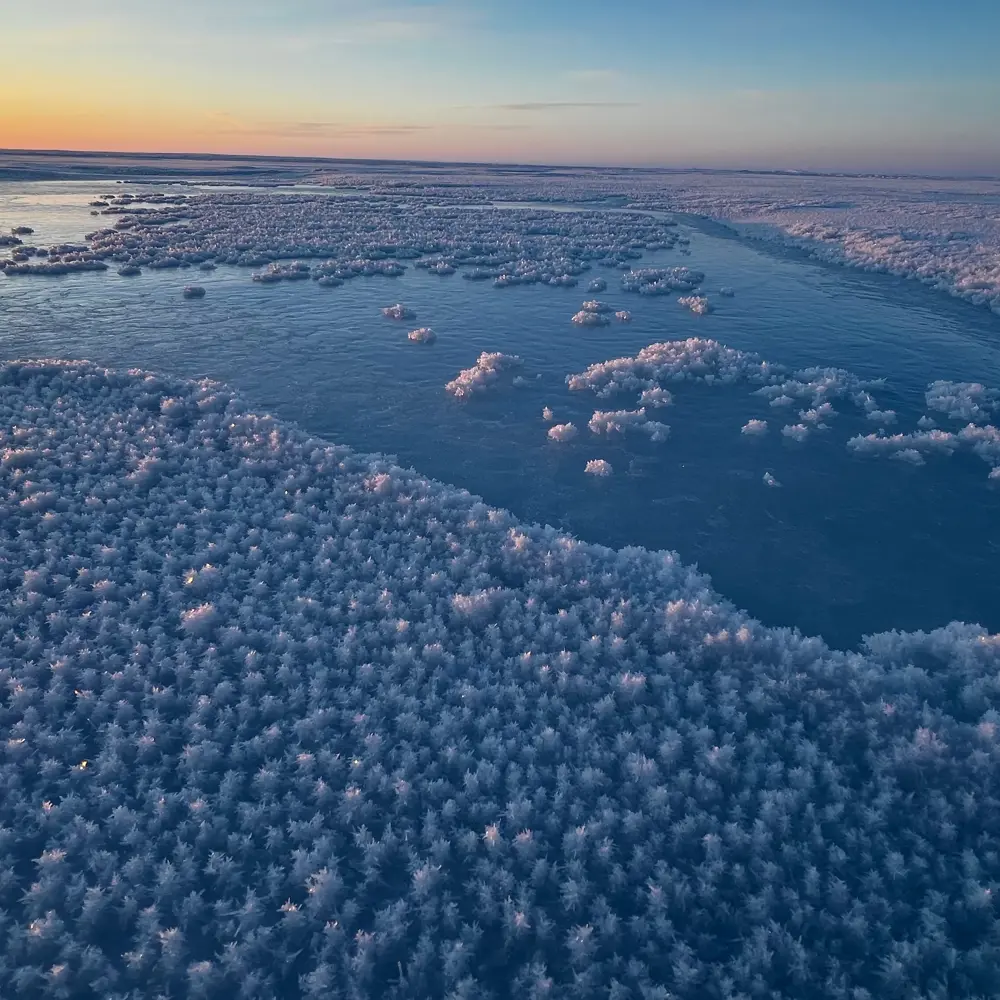 Photo of water on an ice plain starting to freeze with a sunset in the background