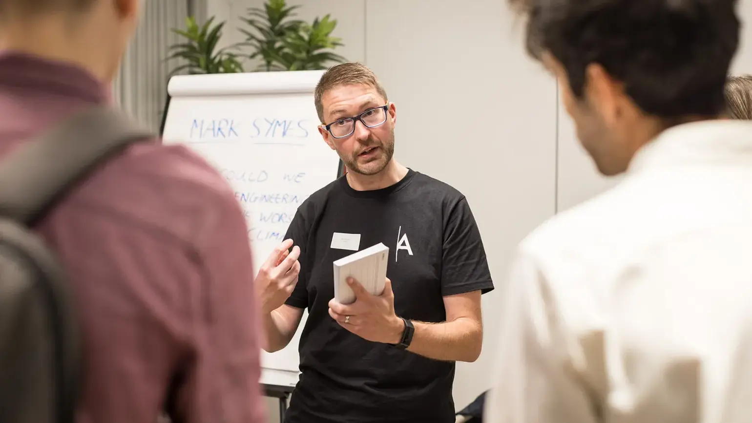 Mark Symes standing in front of a whiteboard speaking to people
