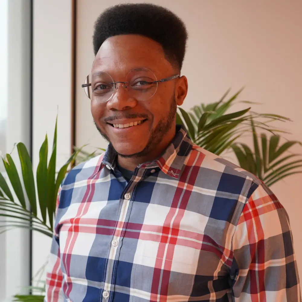 Headshot of David Lewis standing in front of a large window with a plant behind him