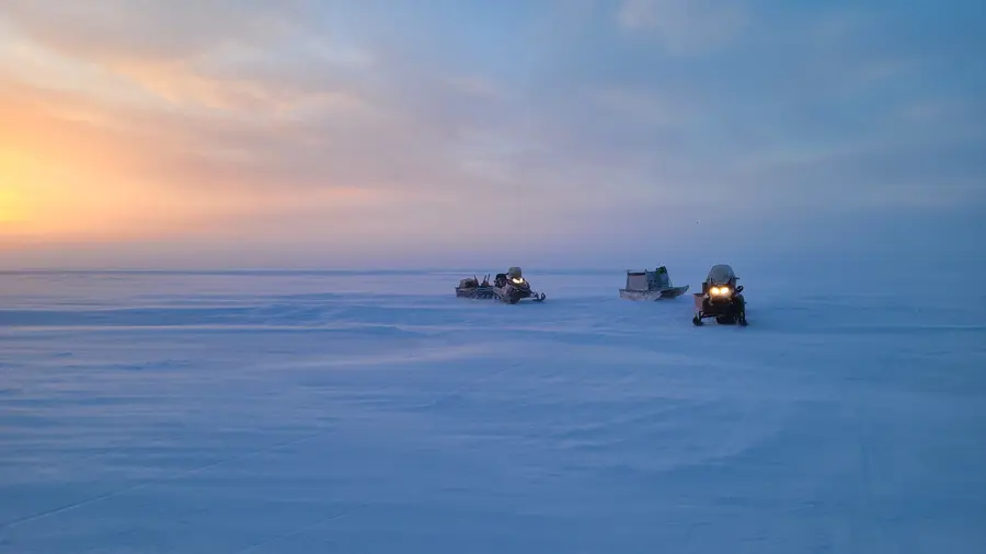 Three snow mobiles sitting on an ice field with a sunset in the background